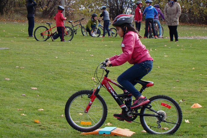 While participating in a bike rodeo with her elementary school, a student demonstrates ready position and control on her bicycle when crossing one of the many elements of the bike playgroun; GreenUP and B!ke will be bringing the bike playground to Peterborough parks this summer (photo: GreenUp)