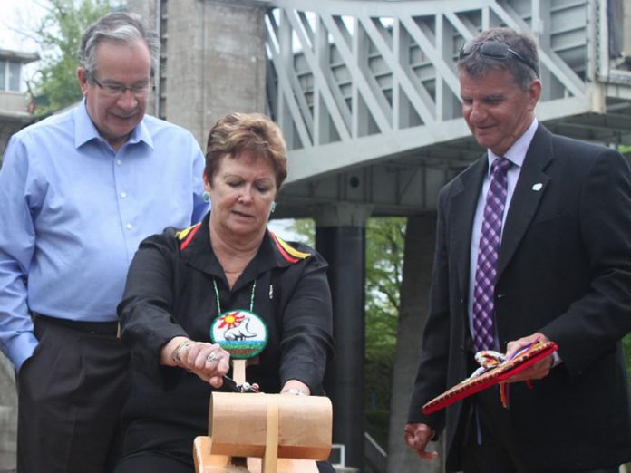 Chief Phyllis Williams of Curve Lake First Nation carving The Canadian Canoe Museum's symbolic paddle while Peterborough MPP Jeaf Leal and Peterborough County Joe Warden look on. The museum is engaging Indigenous peoples throughout the planning process. (Photo: The Canadian Canoe Museum)