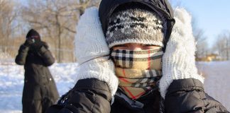 A person in the winter with their face covered and mittened hands over their ears. (Stock photo)