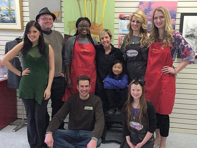 Local celebrities (including two current kawarthNOW writers and one former one) came together at the Art School of Peterborough to create a collaborative painting for the school's annual art auction. Pictured from front to back: Scarlett Grace, Michael Fazackerley, Faith Dickenson, Sam Tweedle, Kemi Akapo, Carol Lawless (with her daughter), Michelle Ferreri, and Christina Abbott.