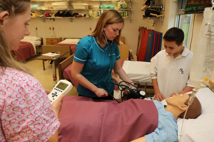 Students Alex Kaczmarek (left), Cassie Peeters (middle), and Nick Goffredo work on a simulated patient in the lab of the Specialist High Skills Major in Health and Wellness program at St. Thomas Aquinas Catholic Secondary School in Lindsay