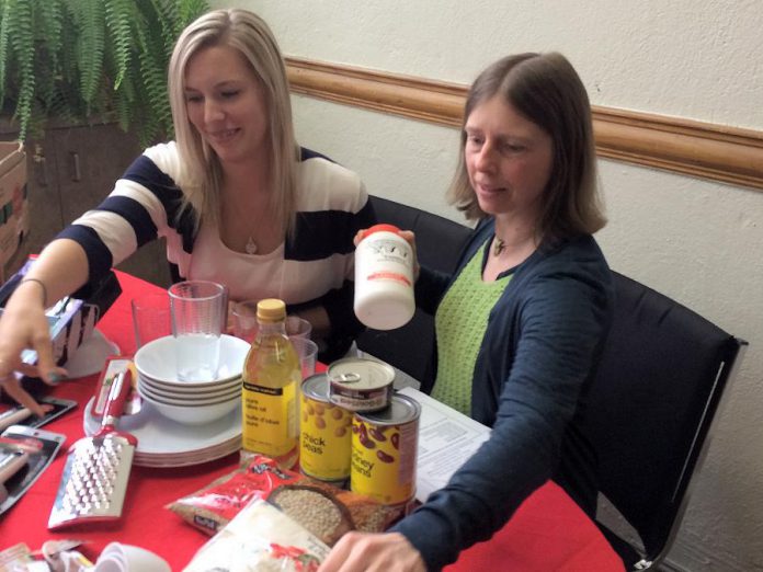 Kawartha Food Share's Ashlee Aitken and NCC's Tamara Hoogerdyk with examples of the food and kitchen-related items they are asking the public to donate to help welcome Syrian refugee families settling in Peterborough (photo courtesy of New Canadians Centre)