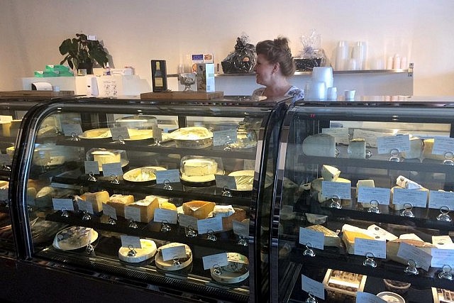 Owner Christel Rumgay prepares a wedge of cheese; Delectable Fine Foods offers an impressive selection of fine cheeses (photo: Eva Fisher / kawarthaNOW)