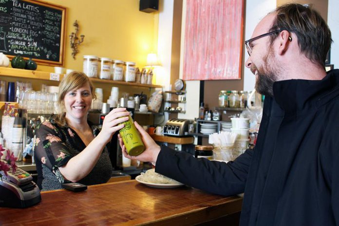 Maggie Lightfoot passes a bottle of tap water over the counter to GreenUP Water Programs Coordinator Dylan Radcliffe at Black Honey Coffee House on Hunter Street, Peterborough. Black Honey is one of many businesses that have signed up as part of BlueWPtbo.ca, an online app mapping businesses in the city where anyone can fill up their reusable water bottle for free. (Photo courtesy of GreenUP)