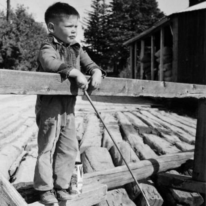 Five-year-old Neil Young in August 1950, fishing from a wooden bridge over the Pigeon River in Omemee. (Photo: Harold Whyte)