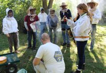 GreenUP's Resident Beekeeper Marcy Adzich shows a group of community members how a hive smoker works at an Open Hive! event at GreenUP Ecology Park in Peterborough while a member of the GreenUP Community Beekeeping Program assists with the demonstration. The hive is smoked so that the bees will not sting when the group enters the hive. (Photo: Karen Halley)