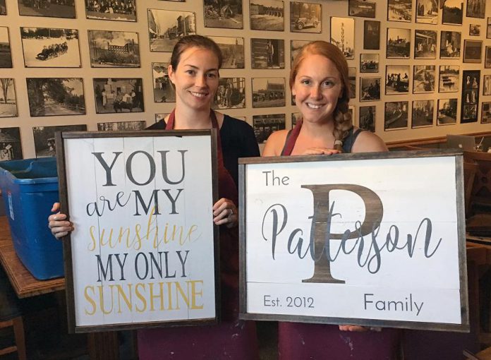 Cheryl Borczak, left, and Cailin Patterson show off their custom-made signs from the workshop at the Black Horse Pub. Before attending the three-hour workshop, participants submit details to Anchor & Co. about what they want on their sign ahead of time, and a personalized stencil is created for them. (Photo: Anchor & Co.)