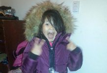 Nova, a child in Kitchenuhmaykoosib Inninuwug First Nation (a fly-in community in the boreal forest of Northern Ontario), reacts as she receives her new donated winter coat. (Photo: Kawartha Truth and Reconciliation Support Group)