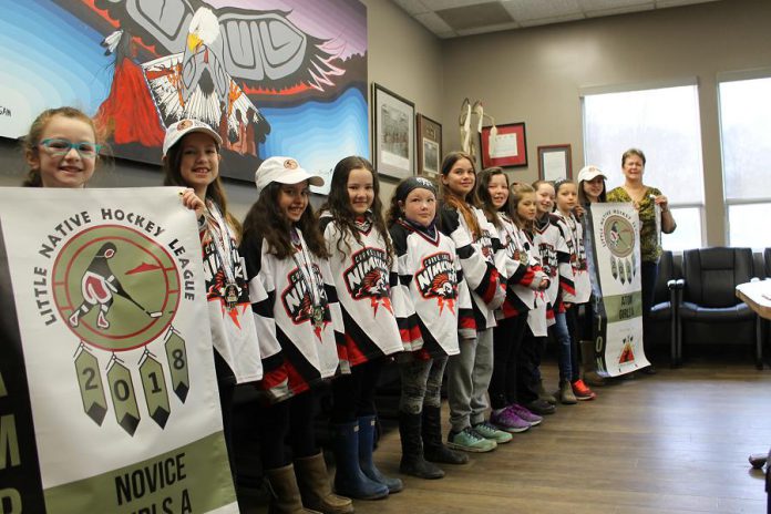Players from the Curve Lake First Nation Nimkiins Kwe Novice Girls and Atom Girls teams display their championship banners to Chief and Council: Danika Jacobs, Maggie Jevons, Sierra Jacobs, Miley Garbutt, Naomi Coppaway, McKenzie Taylor, Goldie Whetung, Brittany Foster, Abigail Jacobs, Kenzie McIntyre, Marissa Williams, and Chief Phyllis Williams. (Photo courtesy of Curve Lake First Nation)