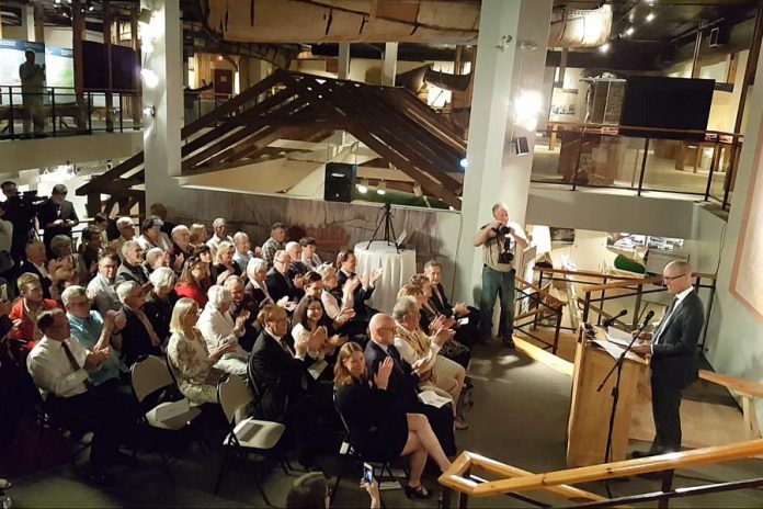 The crowd at The Canadian Canoe Museum applauds after Garfield Mitchell, director of the W. Garfield Weston Foundation and a member of the Weston family, announced a gift of $7.5 million to The Canadian Canoe Museum’s capital campaign to build a new facility on the Trent canal beside the Peterborough Lift Lock. The announcement of the largest ever one-time private gift to a charitable organization based in Peterborough took place on May 16, 2018 at the museum's current location on Monaghan Road in Peterborough. (Photo: Jeannine Taylor / kawarthaNOW.com)