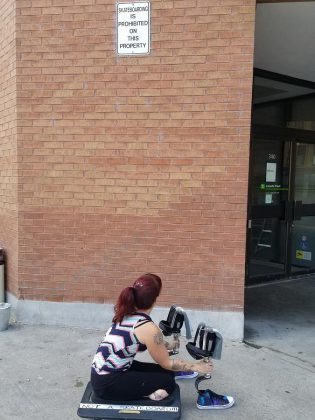 "One question I am exploring is how a non-normative body explores a normative space," says Kingston-based circus artist Erin Ball, who lost her lower legs after a life-changing event. Ball is pictured here under a no-skateboarding sign at Peterborough Square; the platform Ball is using reads "Not a skateboard!!!". (Photo: Patrica Levert-Thorne)