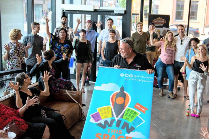 Peterborough DBIA executive director Terry Gueil (holding sign) announced the return of the Win This Space entrepreneurial competition for its third straight year in the lobby of the VentureNorth business hub in downtown Peterborough on September 18, 2018. The winner of the competition will win a free lease for a year of a vacant downtown storefront along with other prizes. (Photo courtesy of the Peterborough DBIA)