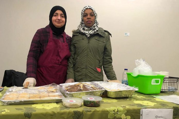 Two members of the Newcomer Kitchen in Peterborough on the first day at the winter location of the Peterborough Regional Farmers' Market in Peterborough Square. The market is donating vendor space for the group of Syrian refugees, who formed the Newcomer Kitchen to sell food including spinach pies, smoky baba ghanoush, and their very popular zaatar bread. (Photo courtesy of New Canadians Centre)