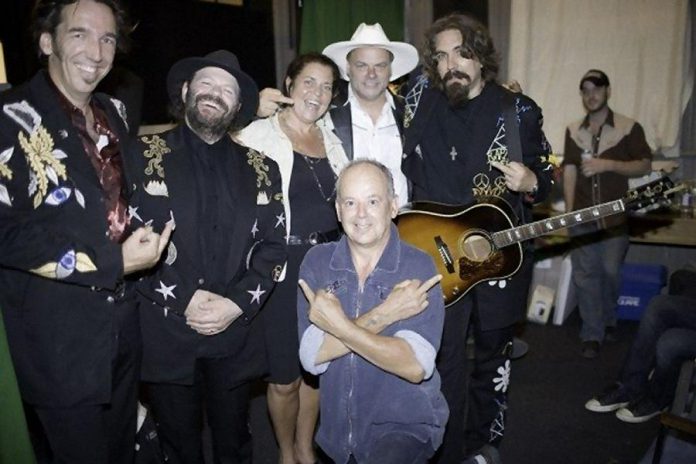 Fred Eaglesmith (in the cowboy hat) giving the all-in-good-fun "Willie P" salute at the July 27, 2007 benefit show at the Market Hall in Peterborough for Fred Eaglesmith's long-time bandmate Willie P. Bennett (front), who had to stop touring after suffering a heart attack (he died six months after this photo was taken of a another heart attack). Also pictured from left to right: Stephen Fearing, Colin Linden, kawarthaNOW.com publisher Jeannine Taylor, and Tom Wilson. (Photo: Rainer Soegtrop)