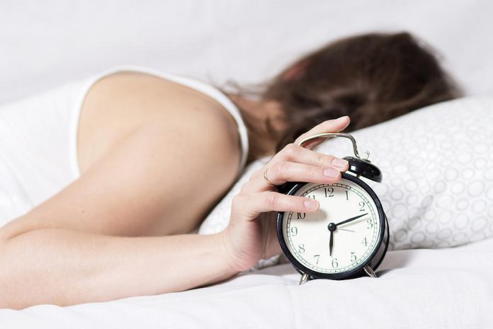 Women in bed with hand on alarm clock