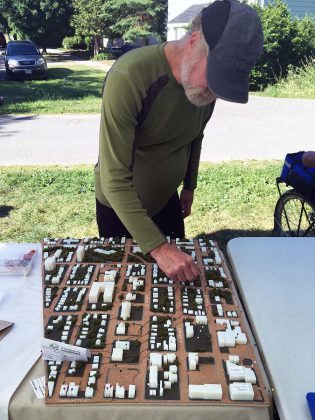 A passersby at a NeighbourPLAN event stops to contribute to the community asset mapping exercise, by placing pins on a 3D model of the neighbourhood to signify where they shop, work, or play, as well as areas of which they are proud or afraid. (Photo: Francis Nasca)