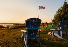 Muskoka chairs beside lake with Canadian flag in background