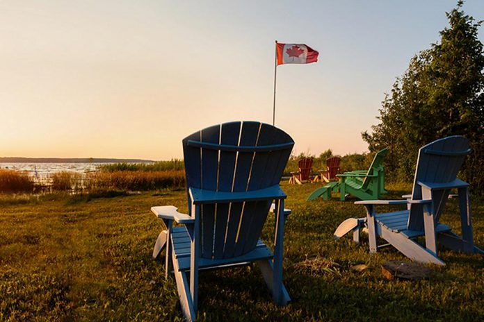 Muskoka chairs beside lake with Canadian flag in background
