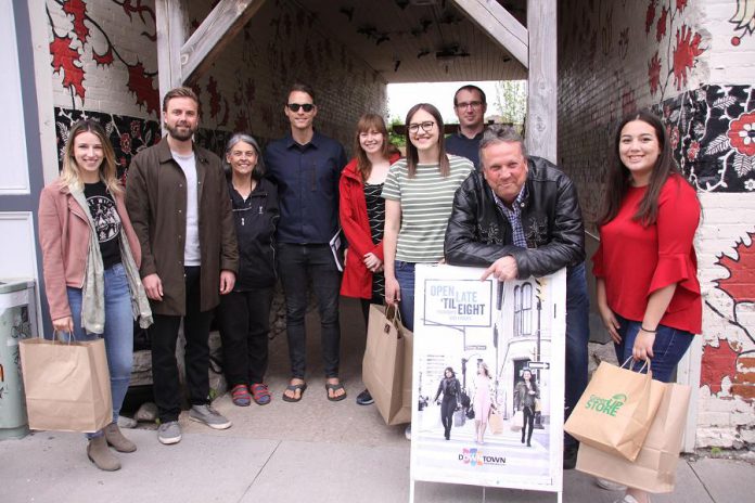 Along with staff and volunteers, Peterborough Business Downtown Improvement Area executive director Terry Guiel points at the promotional signage during the launch of the new 'Open Late 'Til Eight' initiative on June 4, 2019. The initiative will see 27 retail stores in downtown Peterborough staying open until 8 p.m. on Thursdays and Fridays this summer, and parking will be free in the downtown after 6 p.m. (Photo: Jeannine Taylor / kawarthaNOW.com)