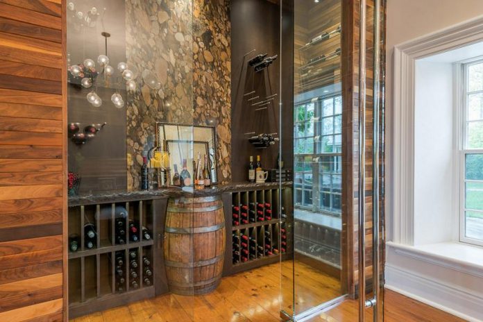 The open glass temperature-controlled wine room is open to the kitchen and family room and features a signature a river rock granite wall in the middle and an oak barrel display table.