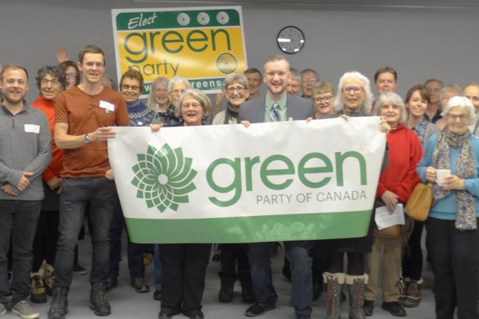 Brock Grills, pictured here (under clock, holding banner) after winning the Peterborough-Kawartha federal Green Party nomination on February 25, 2019, has stepped down as the candidate for personal reasons. (Photo: Peterborough-Kawartha Federal Green Party Association )