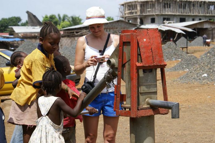 Families in Liberia in West Africa must pay for their children's education. They earn meagre income from selling charcoal, hand-made peanut butter, or other products at the local market, from sewing clothing, or hand cracking rocks to sell to road paving companies. Pictured is volunteer Carolyn Bondy Green showing children photos she took of them, with piles of hand-cracked gravel shown in the background. (Supplied photo)