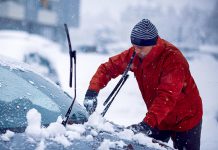 Man clearing snow and ice from car during a winter storm