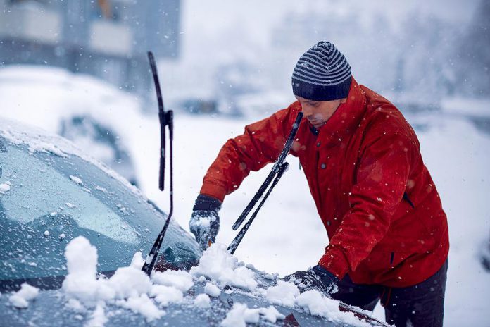 Man clearing snow and ice from car during a winter storm