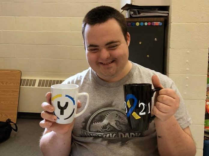 Josh, a member of The Biz Group, displays two of the group's hand-painted mugs created for Y Drive and Peterborough Challenger Baseball. The group is also selling "love mugs" and plans to expand with hand-painted tote bags and t-shirts. All proceeds from the sales of items go directly to members of The Biz Group, an initiative supported by the Down Syndrome Association of Peterborough. (Photo courtesy of Down Syndrome Association of Peterborough)