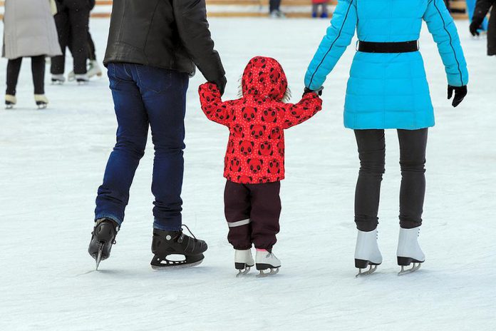 Two parent teaching their young child how to skate on an outdoor rink.