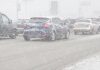 Cars on road during winter storm with snow causing poor visibility.