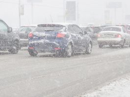 Cars on road during winter storm with snow causing poor visibility.