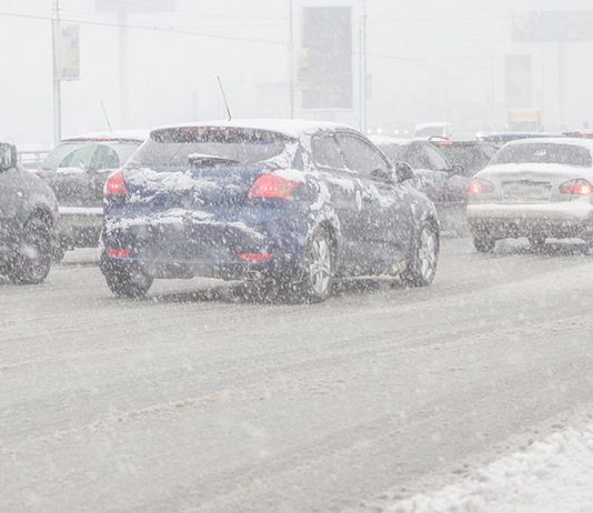 Cars on road during winter storm with snow causing poor visibility.