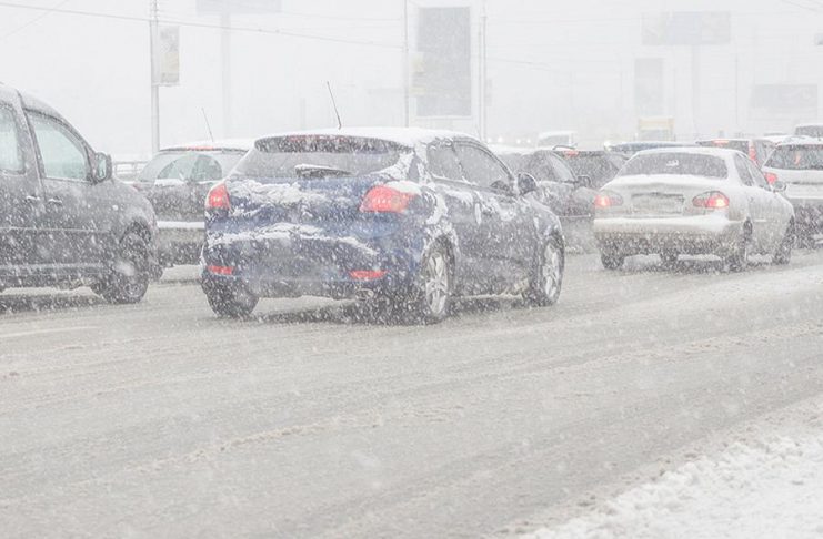 Cars on road during winter storm with snow causing poor visibility.