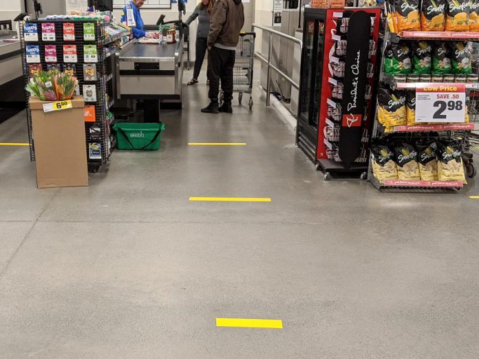 Many grocery stores have already placed a limit on the maximum number of items of any one product that a customer can buy and have dedicated their first hour of operation to serving seniors and those with disabilities. Stores have begun to place floor markers at check-out lines to remind customers of the recommendation for two metres of social distancing and some are installing plexiglass shields for the checkout counters. The Loblaw Real Canadian Superstore at Lansdowne Place in Peterborough has installed social-distancing floor markers at staggered check-out lines, and each customer must wait at a safe distance until the customer ahead of them has completed packing their own groceries. (Photo: Bruce Head / kawarthaNOW.com)