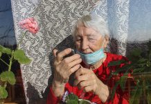 An elderly woman at home wearing a mask looking at her phone