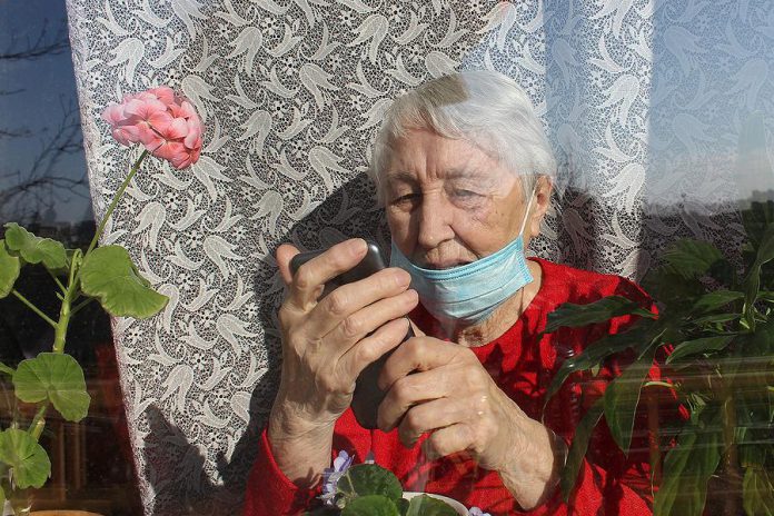 An elderly woman at home wearing a mask looking at her phone