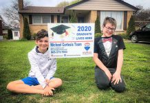 Port Hope artist Lee Higginson's sons Sam and Charley, who were both scheduled to have graduation ceremonies this year, with a sign provided by Cobourg real estate broker Michael Cortesis to help celebrate their graduations. (Photo: Lee Higginson / Facebook)