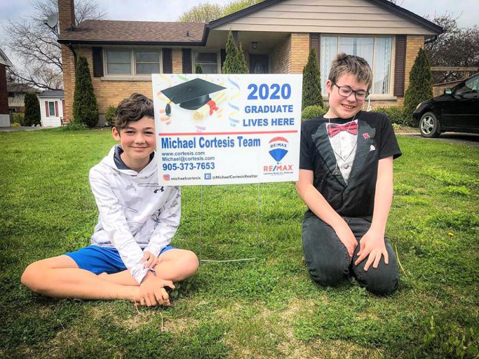 Port Hope artist Lee Higginson's sons Sam and Charley, who were both scheduled to have graduation ceremonies this year, with a sign provided by Cobourg real estate broker Michael Cortesis to help celebrate their graduations. (Photo: Lee Higginson / Facebook)