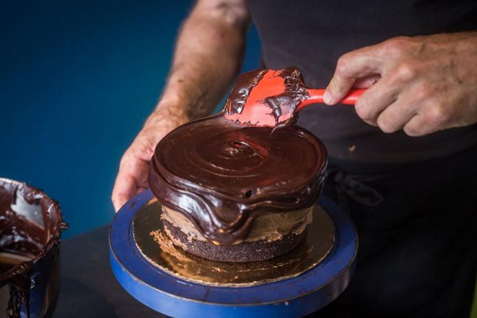 Bill Reddick using a potter's wheel to help ice his gluten-free chocolate cake. Reddick decided to turn his cakes into a business after he lost income as an artist during the COVID-19 pandemic.  (Photo: Bill Reddick / Instagram)