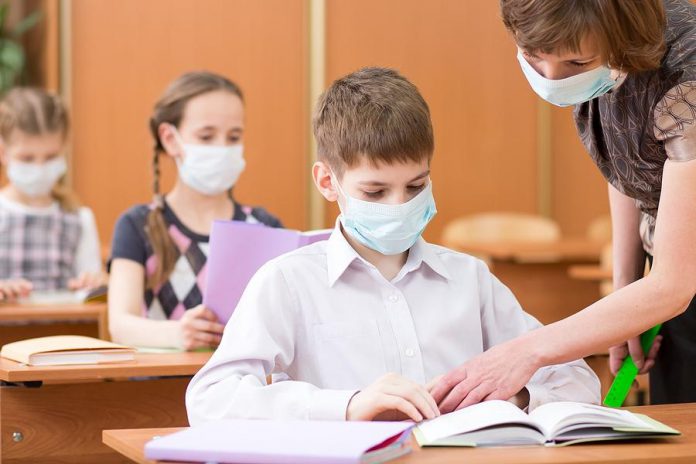Students in a classroom and their teacher wearing face masks. (Stock photo)