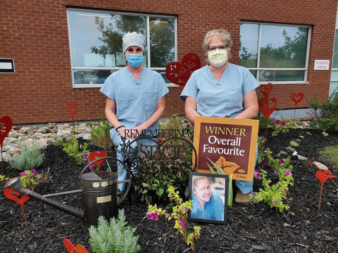 Theresa Connell and Marlene Dawson of Ross Memorial Hospital in Lindsay, two colleagues of late emergency department nurse Stacie Vokins, stand in the garden they dedicated to the memory of Vokins (shown in the picture frame), a 20-year employee of the hospital who passed away in November 2019. The garden, which includes heart sculptures by local artist Christina Handley, won the hospital's annual "Garden Cup". (Photo courtesy of Ross Memorial Hospital)