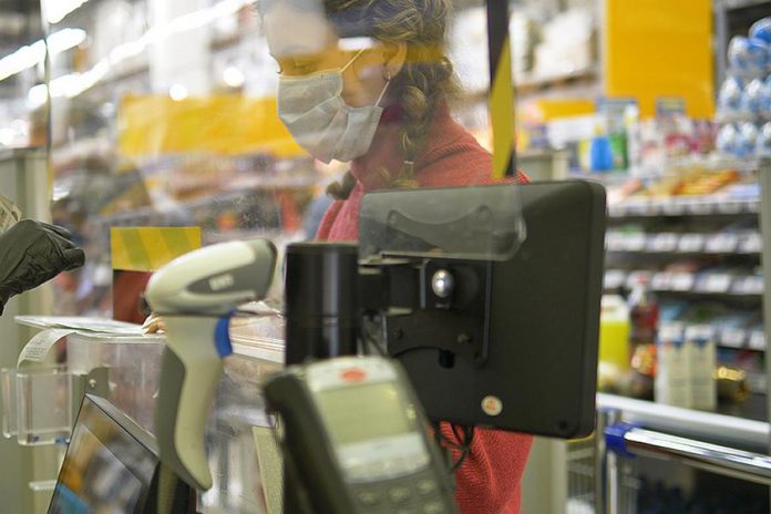 A cashier wearing a fask mask while behind a plexiglas shield. (Stock photo)