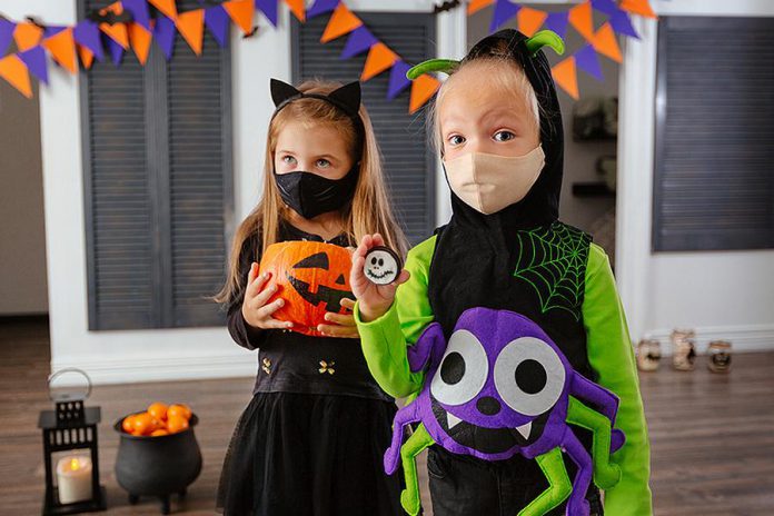 Two children wearing COVID-19 face coverings and Halloween costumes. (Stock photo)