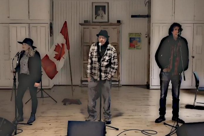 Melissa Payne, Neil Young, and Travis Good singing harmony vocals to Bob Young's song "Hey America". Due to the pandemic, the three musicians were filmed separately using the same background, and the shots were assembled in post-production to make it appear they were singing together. (Screenshot)