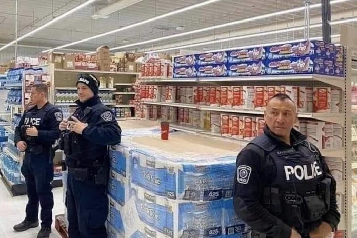 Police officers at an unidentified location in Canada protect a skid of toilet paper. (Photo source: jkooshan / reddit.com)