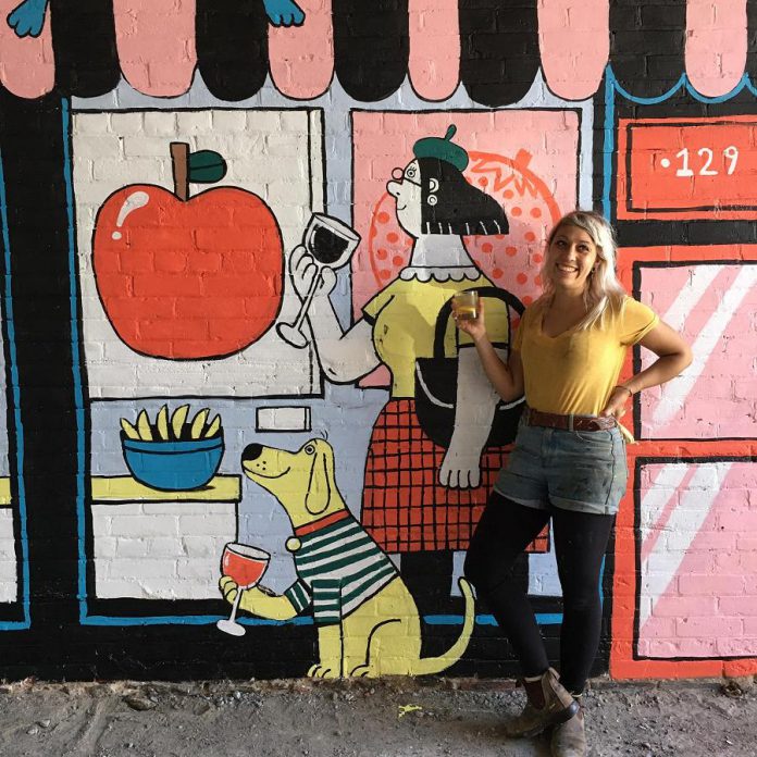 Peterborough illustrator Kathryn Durst in front of her public art mural in the alleyway of the Commerce Building in downtown Peterborough. The mural, commissioned by the First Friday Peterborough volunteer committee and Commerce Building owner Ashburnham Realty, was celebrated on September 4, 2020. (Photo: First Friday Peterborough / Facebook)