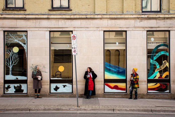 Former Toronto artist Julii McMillan (middle), who is now living in Peterborough, is one of the founders of the "Neighbourhood Love" public art campaign, launched this fall in Etobicoke when a family received hate mail after having a mural commissioned on their garage door. McMillan has joined with local artists Bethany LeBlonc (left), Dawn Pond, Brooklin Stormie, and Olivia Chessman and Toronto artists Julia Prajza and Bareket Kezwer (right) to paint six window murals in downtown Peterborough as part of the "Love for the Boro" initiative, including this mural at the old Patch Store at Hunter and George. (Photo courtesy of Love for the Boro)