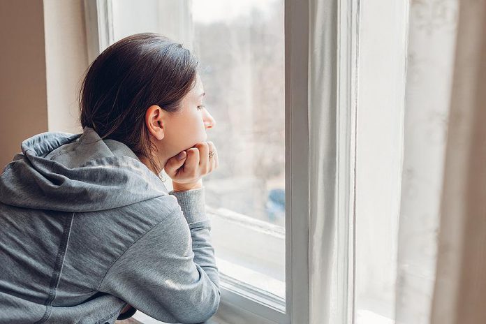 A woman at home looks out of her window. (Stock photo)