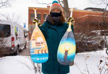 Dawn Pond, Downtown Vibrancy Manager of the Peterborough Downtown Business Improvement Area, displays two of the 20 paddles painted by volunteer community artists to raise funds for the One City Employment Program, which provides meaningful work to those with barriers to traditional employment. The paddles will be on display in the Commerce Building in downtown Peterborough as part of the First Friday Peterborough art crawl. (Photo courtesy of Peterborough DBIA)